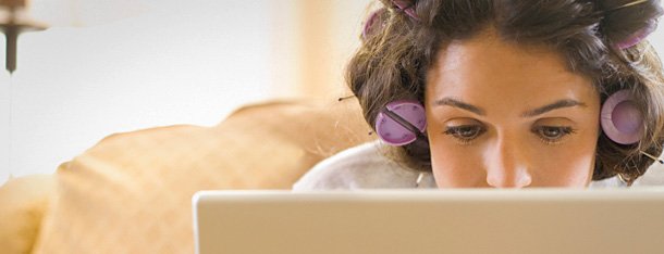 Frau mit Lockenwickler vertieft in ihren Laptop erkundigt sich darüber welche Fehler sie auf der Online Partnersuche vermeiden sollte