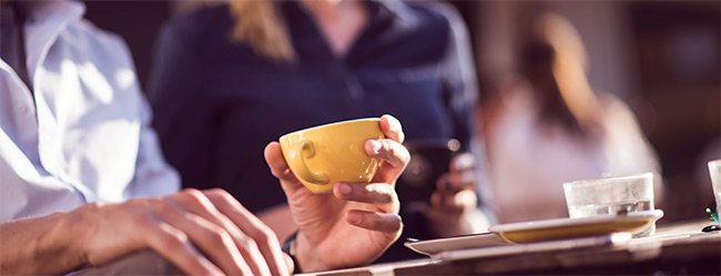 Mann hebt Kaffeetasse im Gespräch mit einer Frau und nutzt Fragen als Waffe in der Kommunikation