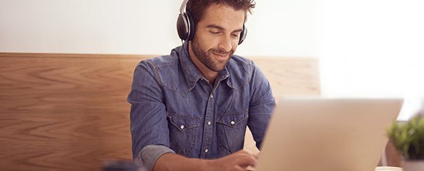 Mann mit Kopfhörern am Laptop profitiert von Profilservice bei ElitePartner