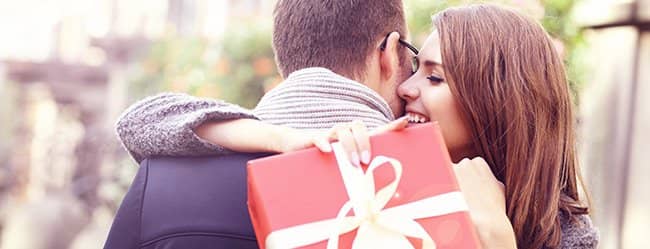Date Geschenk: Frau umarmt Mann und hat Geschenk in der Hand