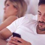Smartphones belasten die Beziehung dargestellt durch ein Paar das im Bett jeweils vertieft ins Handy ist