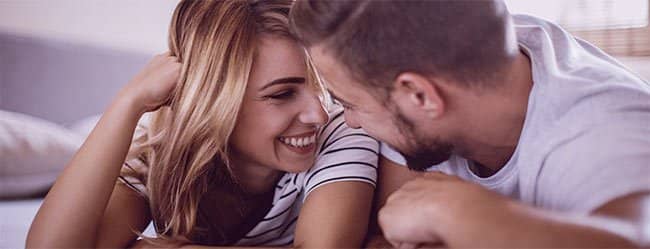 Mann und Frau in einer Rebound-Beziehung liegen auf dem Bauch und lächeln sich an.