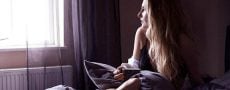Frau sitzt verzweifelt im Bett und blickt aus dem Fenster um herauszufinden wie sie Trennung verarbeiten kann