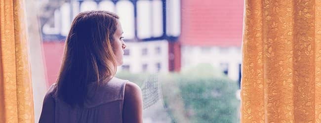 Frau schaut aus dem Fenster als Symbol für emotionale Abhängigkeit