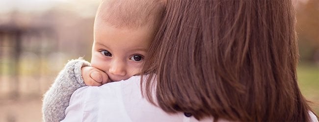 Frau zum Rücken zur Kamera hat Kind auf dem Arm das in Kamera schaut als Symbol für den Kinderwunsch in einer Beziehung