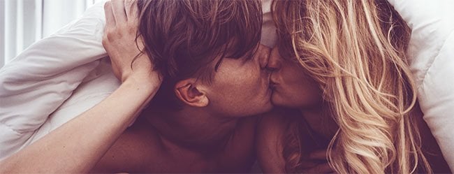 Mann und Frau unter der Bettdecke küssen sich leidenschaftlich als Symbolbild für Sexualität in der Partnerschaft