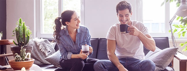 Ein Paar trinkt zu Hause einen Kaffee, er schaut unsicher zu Boden