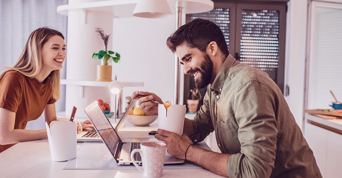 Ein Paar sitzt gemeinsam in der eigenen Wohnung im Homeoffice, für ihre Beziehung hat es sich positiv ausgewirkt, denn sie lachen