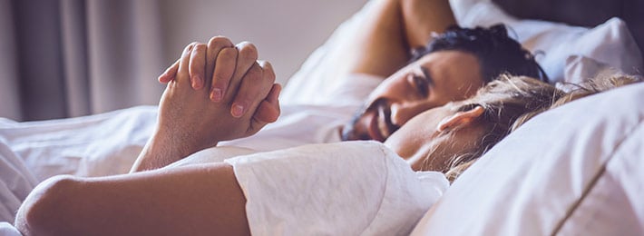 Ein Paar liegt im Bett und hält Händchen als Symbol für Vertrautheit und Nähe bei gutem Sex