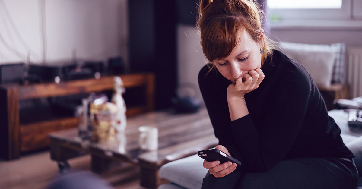 Eine Frau schaut nachdenklich auf ihr Smartphone, ihr Date meldet sich nur selten von sich aus, ein klares Warnsignal beim Dating und Kennenlernen