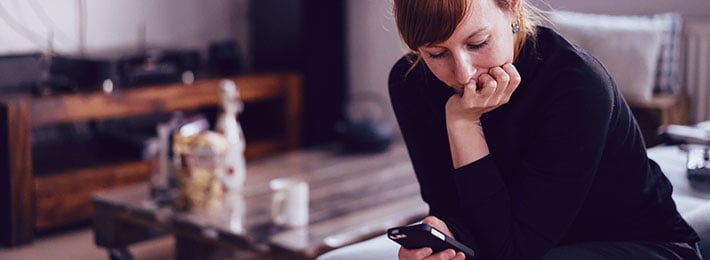 Eine Frau schaut nachdenklich auf ihr Smartphone, ihr Date meldet sich nur selten von sich aus, ein klares Warnsignal beim Dating und Kennenlernen