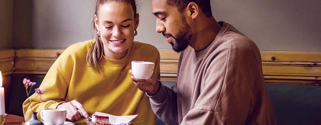 Zwei Singles beim Dating im Café, beide lächeln schüchtern, möchten aber die Absichten ihres Gegenübers wissen