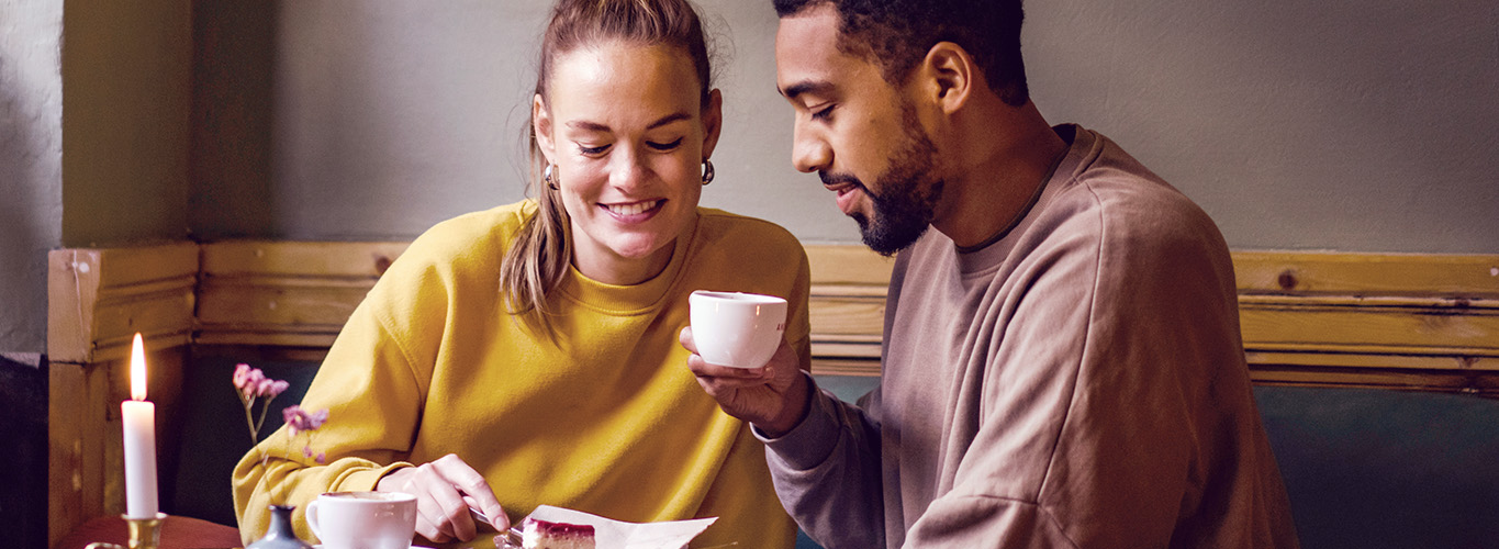 Zwei Singles beim Dating im Café, beide lächeln schüchtern, möchten aber die Absichten ihres Gegenübers wissen