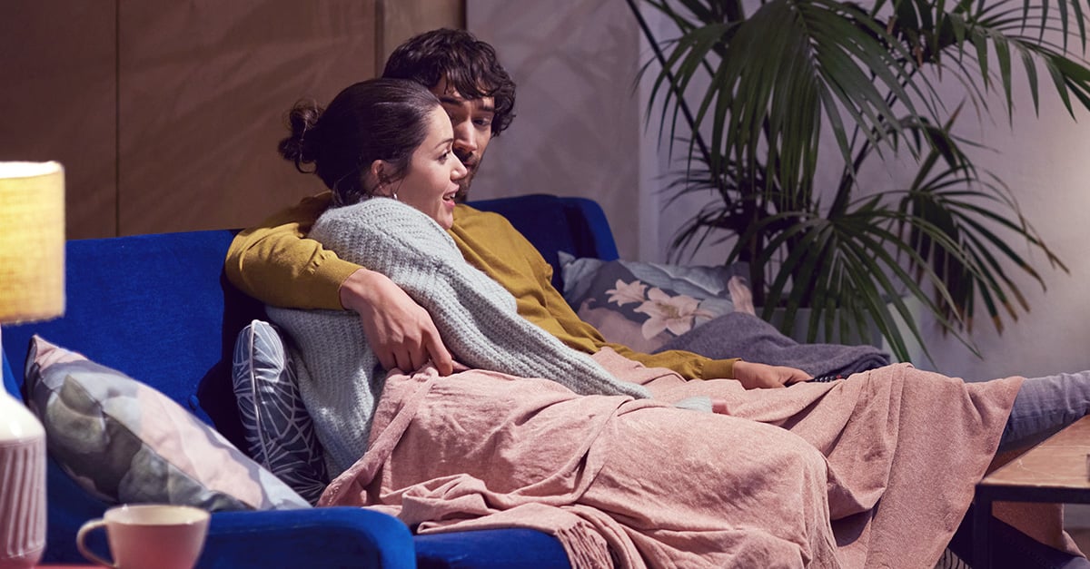 Ein Paar liegt gemeinsam auf dem Sofa, ein Symbol für Bindungserfahrungen in Beziehungen.
