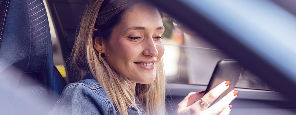 Eine Frau sitzt im Auto und schaut lächelnd auf ihr Handy