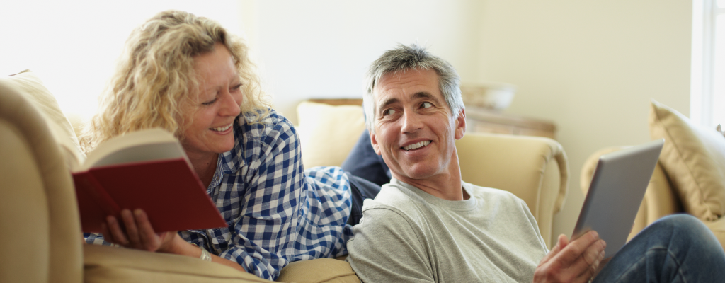 Ein Mann und eine Frau lesen auf dem Sofa, sie lächeln sich an.