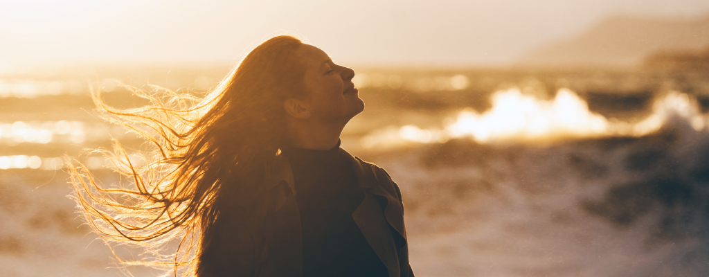 Eine Frau lächelt glücklich, im Hintergrund das Meer.