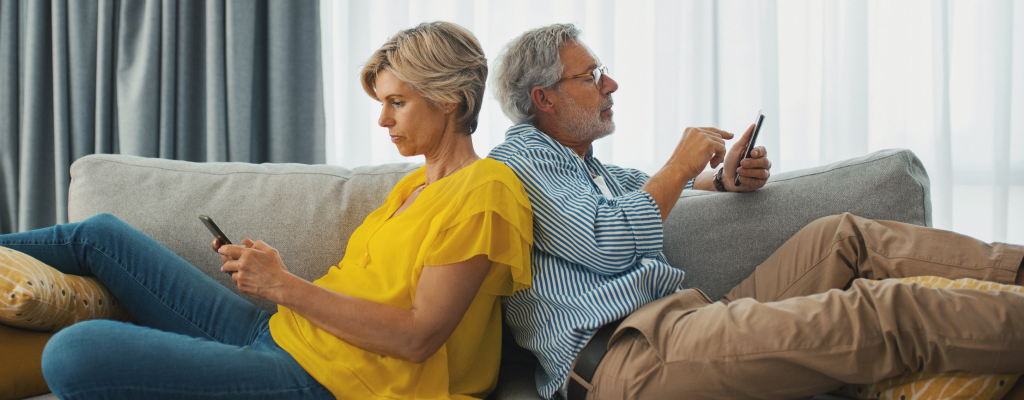 Eiene Frau und ein Mann siztzen Rücken an Rücken auf einem Sofa und benutzen ihre Handys.